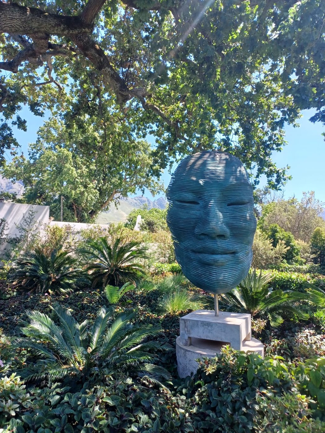 Blue beaded head sculpture in the garden at Muratie wine estate under oak trees